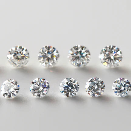 A collection of round-cut Moissanite gemstones arranged on a white background, showcasing variations in brilliance, fire, and color grading.